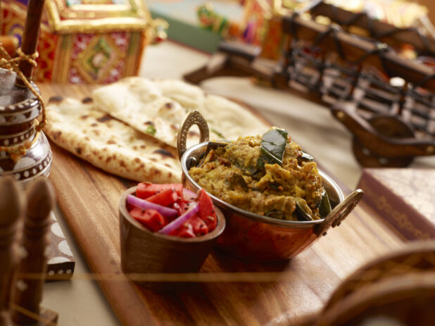 Copper Bowl of Vegetable Poha on a Wooden Platter with Fresh Naan Bread and a Bowl of Pickled Vegetables in an Indoor Setting