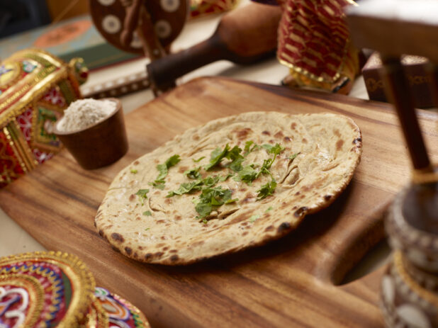 Laccha Paratha - Indian Layered Dough Bread - with chopped coriander leaves on a Wooden Cutting Board in an Indoor Setting