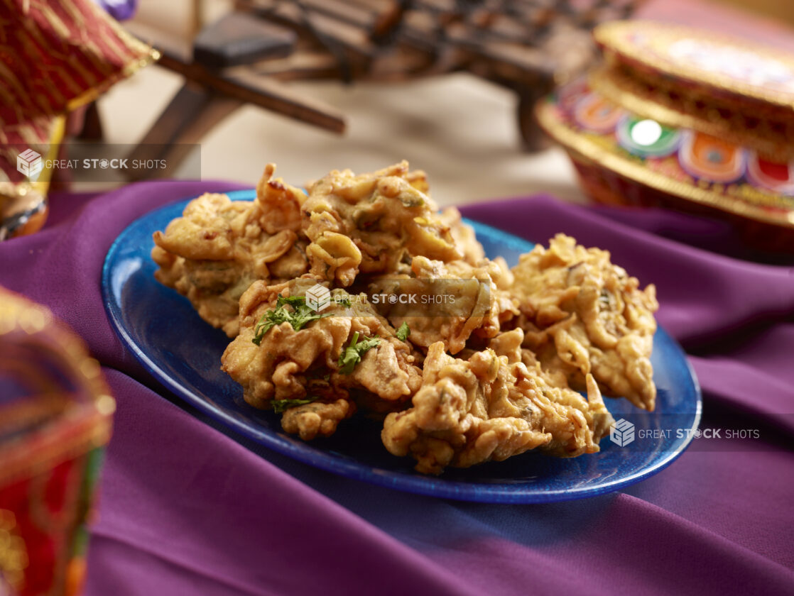 Indian Savoury Snack – Onion Pakoras – on a Blue Ceramic Plate on a Purple Tablecloth in an Indoor Setting