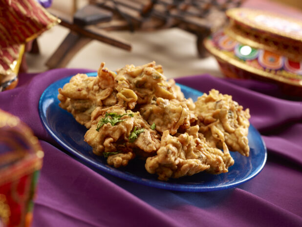 Indian Savoury Snack – Onion Pakoras – on a Blue Ceramic Plate on a Purple Tablecloth in an Indoor Setting
