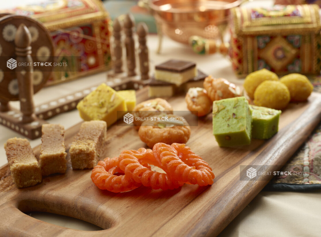 Group Shot of Colourful Assorted Indian Sweets on a Wooden Platter in an Indoor Setting