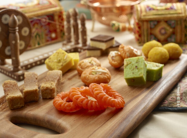 Group Shot of Colourful Assorted Indian Sweets on a Wooden Platter in an Indoor Setting