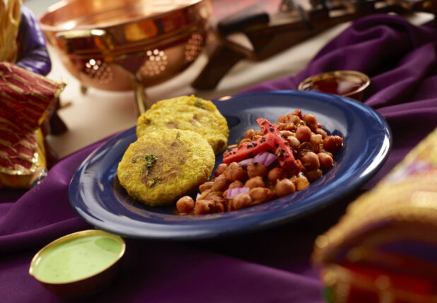 Indian Savoury Snack – Aloo Tikki – with Channa Masala Curry on a Blue Ceramic Plate on a Purple Tablecloth in an Indoor Setting