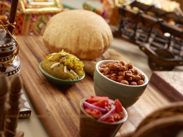 Indian Breakfast of Channa Bhatura - Spiced Chickpeas and Indian Puff Bread with Sooji Halwa Dessert and Pickled Vegetables on a Wooden Tray