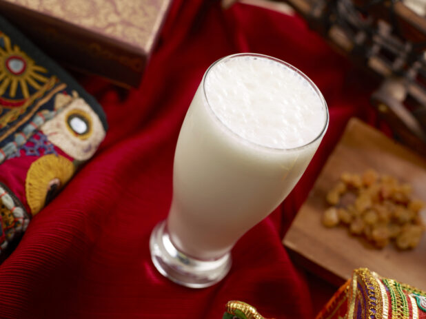 Tall Glass of Lassi – an Indian Yogurt-Based Beverage – on a Red Tablecloth in an Indoor Setting