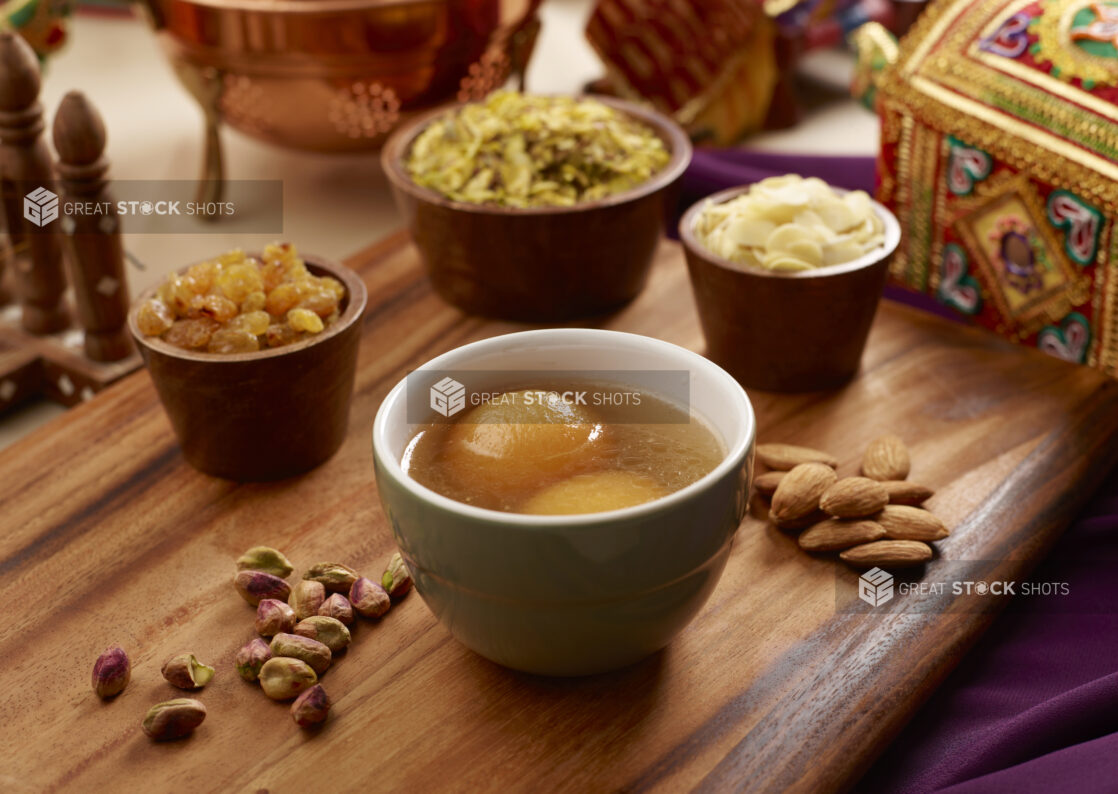 Indian Dessert Gulab Jamun - Fried Milk Dough in Sweet Sugar Syrup with Nuts and Dried Fruit Toppings on a Wooden Platter