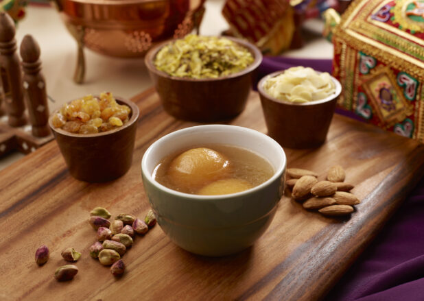 Indian Dessert Gulab Jamun - Fried Milk Dough in Sweet Sugar Syrup with Nuts and Dried Fruit Toppings on a Wooden Platter