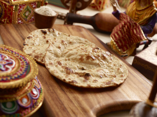 Oven-baked (Tandoor) Butter Naan - Indian Bread on a Wooden Cutting Board in an Indoor Setting