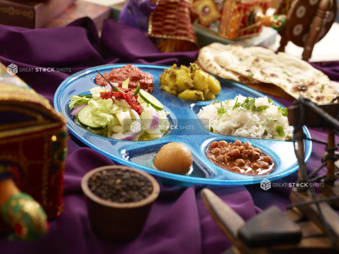 Indian Thali - Combo Platter of Assorted Curries, Rice, Salad and Dessert with Naan on a Purple Tablecloth in an Indoor Setting