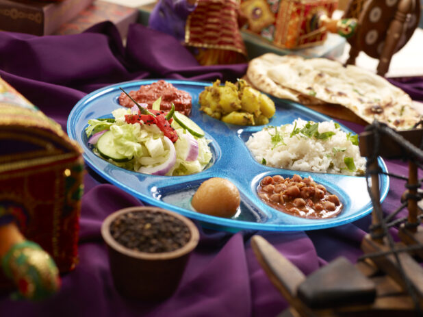 Indian Thali - Combo Platter of Assorted Curries, Rice, Salad and Dessert with Naan on a Purple Tablecloth in an Indoor Setting