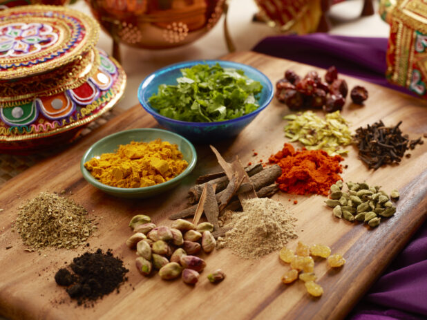 A Colourful Array of Assorted Spices, Nuts and Dried Fruit for Indian Cuisine on a Wooden Platter in an Indoor Setting