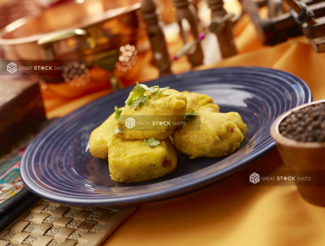 Paneer Pakora - Indian Cheese Fritters - on a Blue Ceramic Plate on an Orange Tablecloth in an Indoor Setting