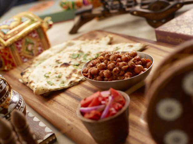 Indian Breakfast of Naan and Chana Masala - Spicy Chickpeas - with a Side Dish of Pickled Vegetables on a Wooden Platter in an Indoor Setting