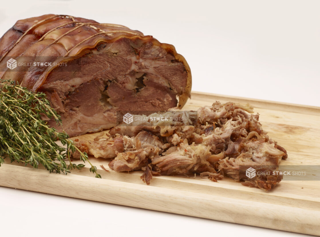 Close Up of Italian Porchetta Roast and Shaved Pork Pieces on a Wooden Cutting Board with Fresh Herbs Isolated on a White Background