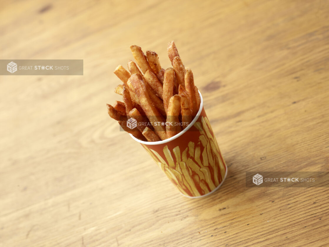 Cardboard Cup of Seasoned Spicy French Fries on a Rustic Untreated Wood Surface