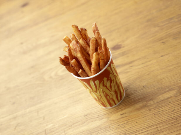 Cardboard Cup of Seasoned Spicy French Fries on a Rustic Untreated Wood Surface