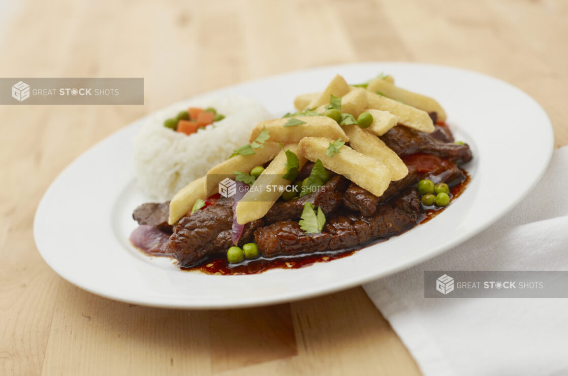 Strip Steak and Fries with Au Jus and a Side of White Rice on a Round White Ceramic Dish on a Light Wooden Table