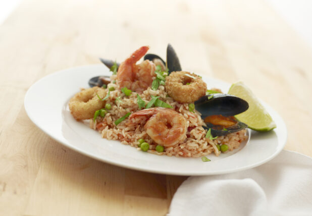 Seafood Jambalaya with Mussels, Shrimp and Deep Fried Squid Calamari and a Lime Wedge on a Round White Ceramic Dish on a Light Wooden Surface