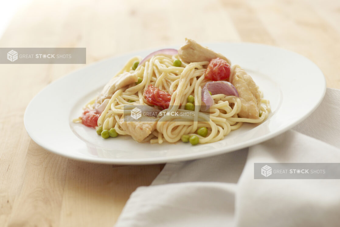 Tomatoes, Green Peas and Chicken Creamy Pasta on a Round White Ceramic Dish on a Light Wooden Surface