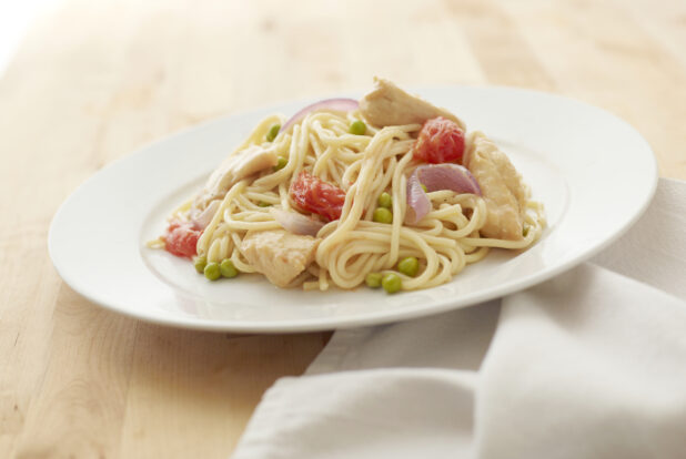 Tomatoes, Green Peas and Chicken Creamy Pasta on a Round White Ceramic Dish on a Light Wooden Surface