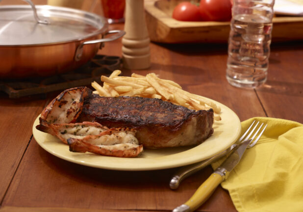 Surf and Turf Dinner Plate with Steak, Lobster Tails and French Fries on a Restaurant Table Setting