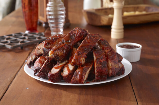 A Platter of Sliced Barbecue Baby Back Ribs and a Side Dish of BBQ Sauce on a Wooden Table in an Indoor Setting