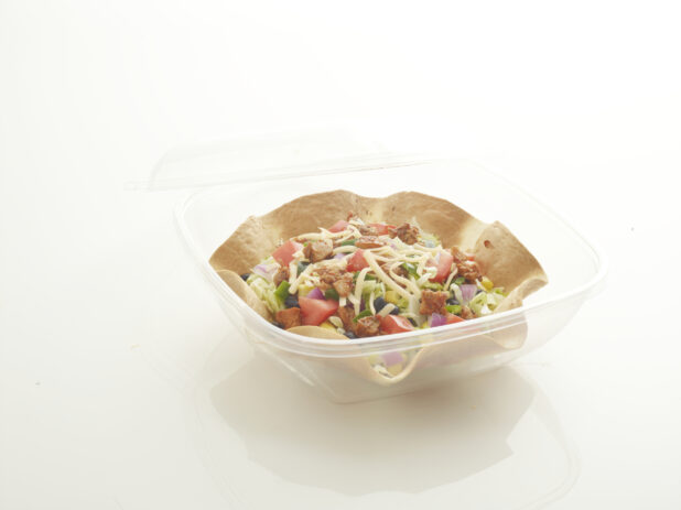 Spicy Grilled Chicken Mexican Taco Salad in a Crispy Tortilla Bowl with a Clear Plastic Take-Out Container on a White Background for Isolation