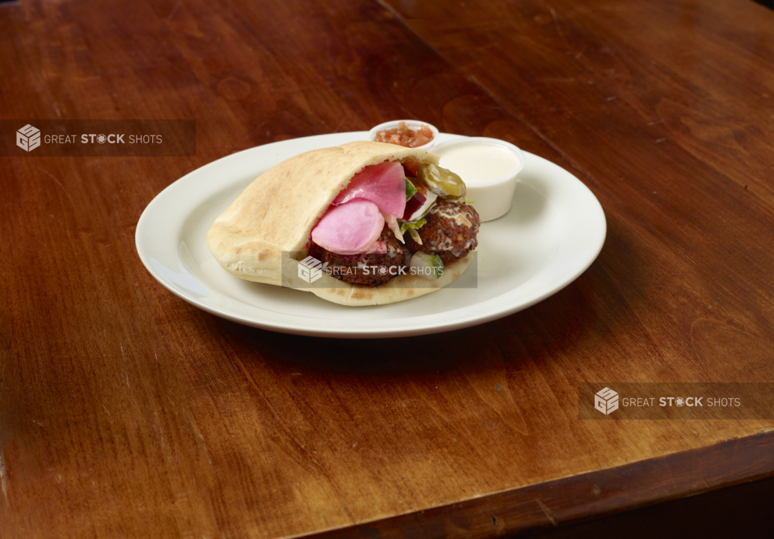 Falafel sandwich showing fresh ingredients on a white plate on a wood table