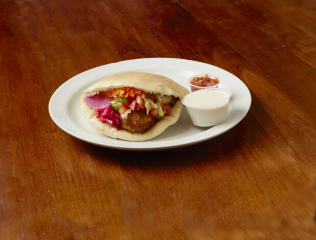 Falafel sandwich showing fresh ingredients on a white plate on a wood table