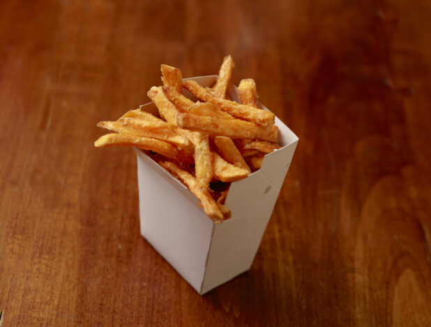 New York style french fries in a white cardboard carton on a wood tabletop