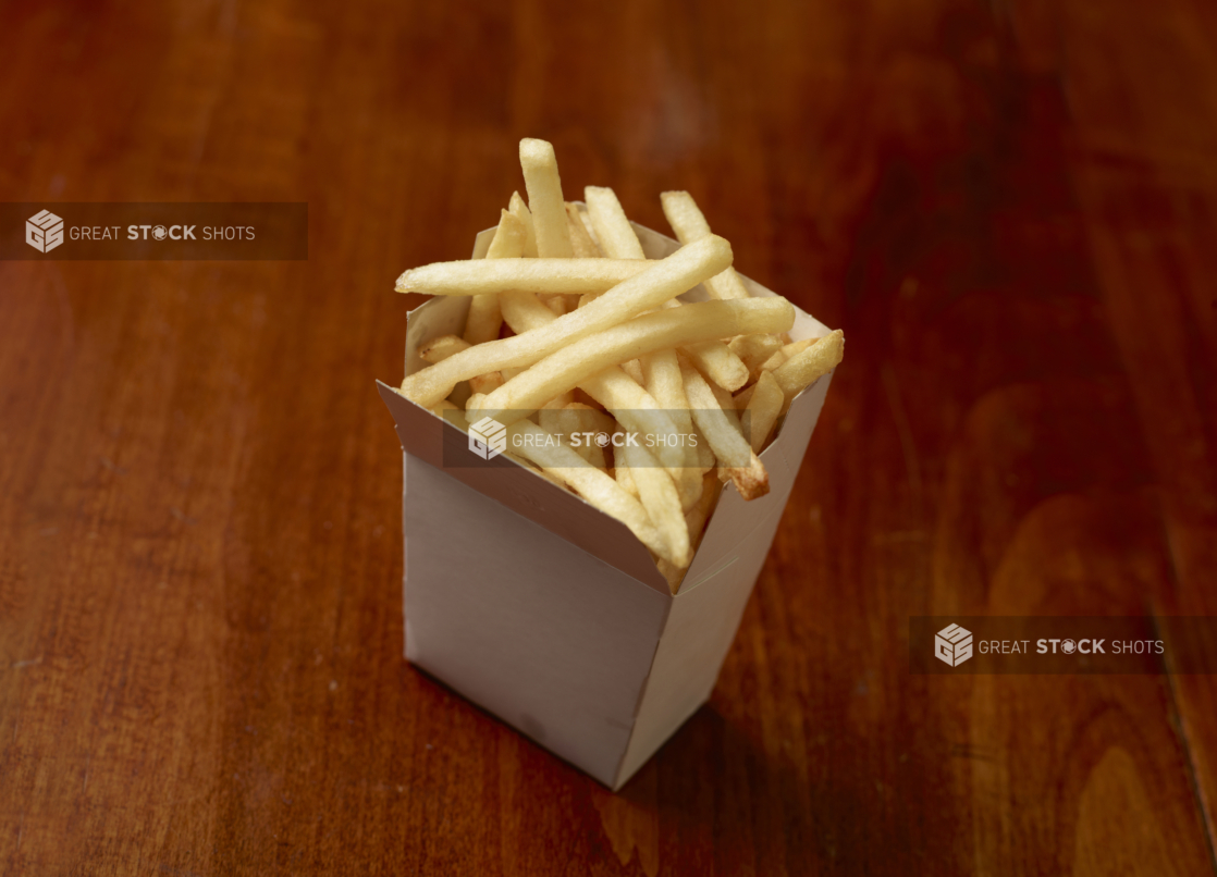 French fries in a white cardboard carton on a wooden tabletop