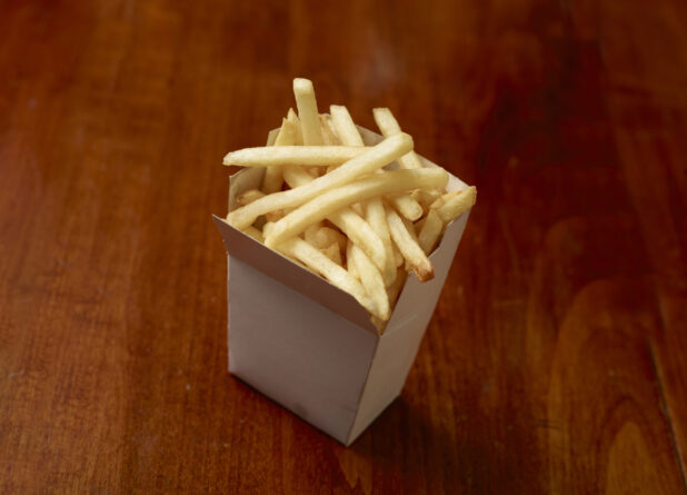 French fries in a white cardboard carton on a wooden tabletop