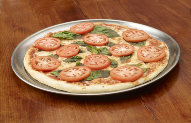 Whole unsliced pizza with basil and slices of tomato