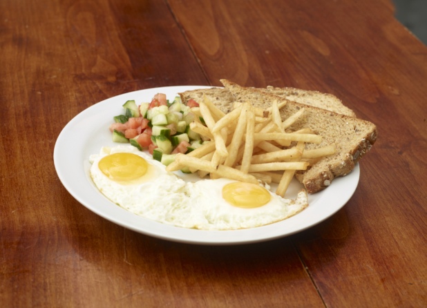 Two eggs sunny side up with french fries, multigrain toast, and chopped tomato and cucumber salad