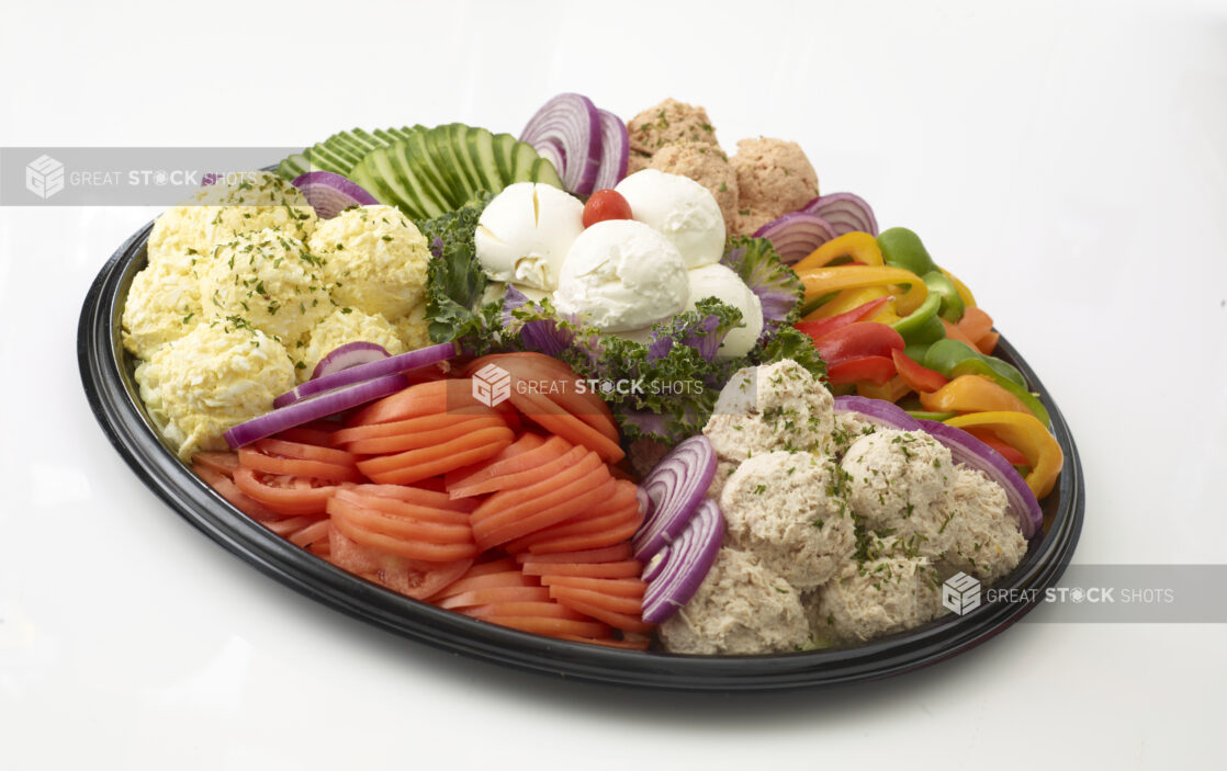 Dairy Platter with tuna salad, egg salad, salmon salad and cream cheese in mounds with sliced tomato, sliced cucumber, sliced red onions and slices of bell pepper all on a black catering tray