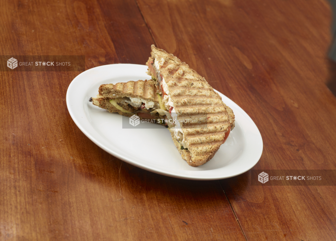 Pressed grilled vegetable sandwich with goat cheese on a white plate on a wood tabletop