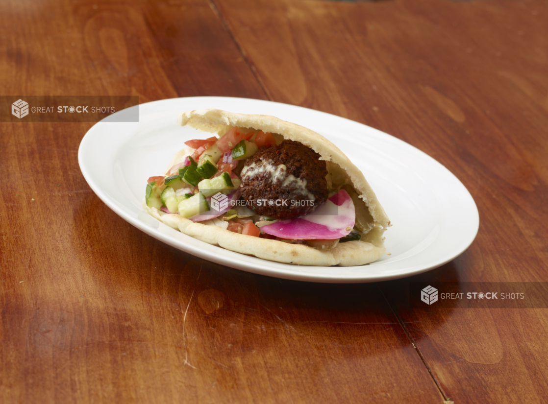 Falafel sandwich showing fresh ingredients on a white plate on a wood table