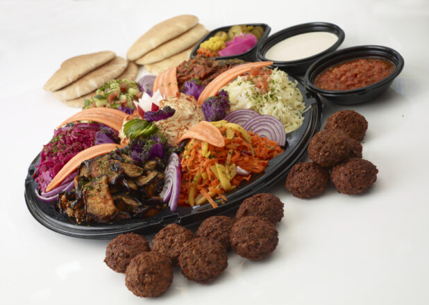 Middle Eastern vegetarian platter with dips, roasted vegetables and salads all on a round black tray with falafel in the foreground and dips and pita in the background