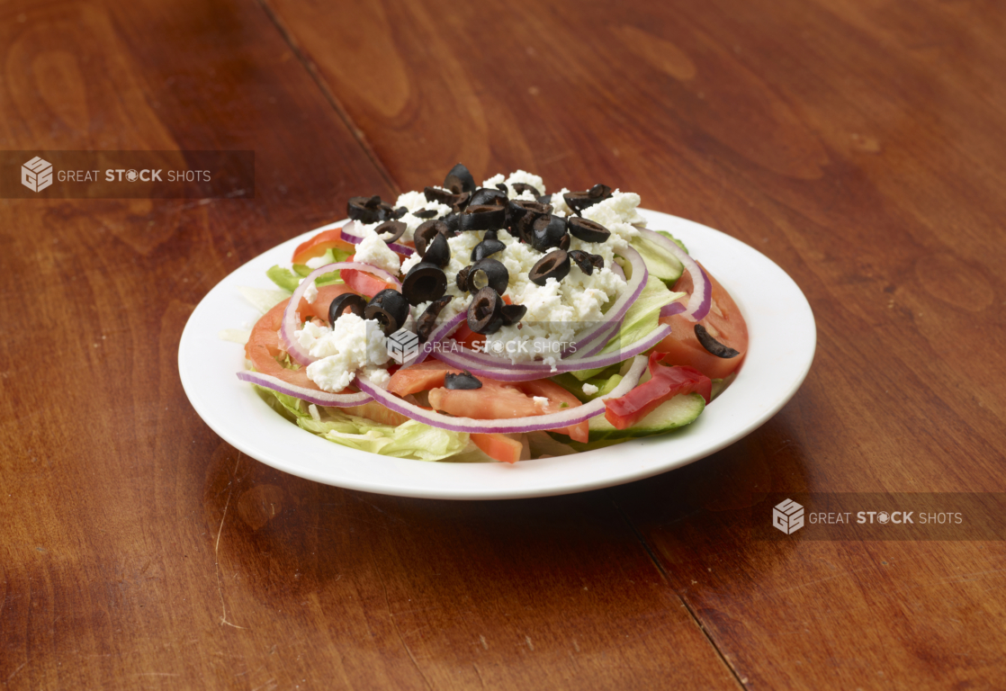 A Classic Greek Salad Topped with Feta Cheese and Black Olives on a White Ceramic Dish on a Wooden Table