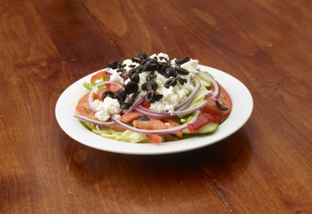 A Classic Greek Salad Topped with Feta Cheese and Black Olives on a White Ceramic Dish on a Wooden Table