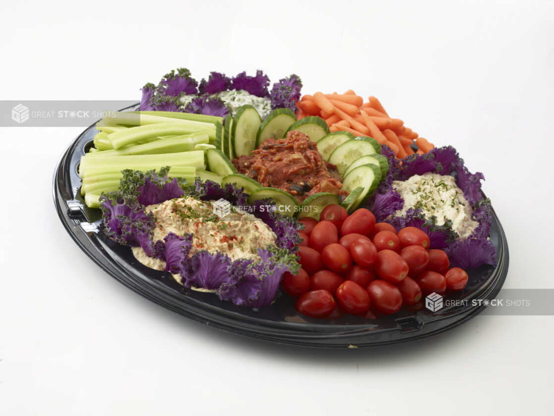 Vegetable and dip platter with 4 dips, fresh grape tomatoes, celery and baby carrots all on a round black tray,