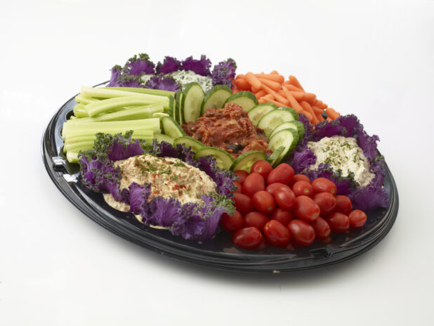 Vegetable and dip platter with 4 dips, fresh grape tomatoes, celery and baby carrots all on a round black tray,