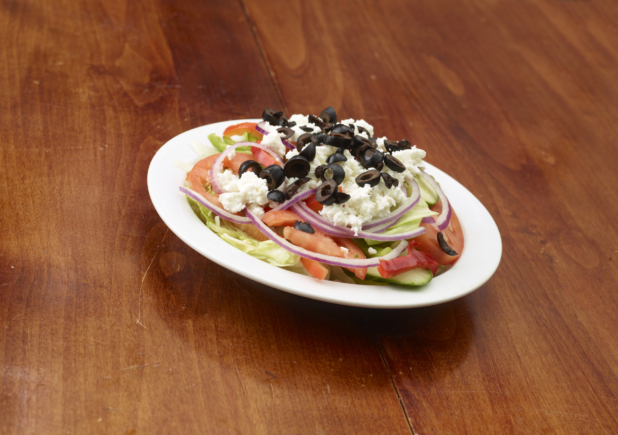 A Classic Greek Salad Topped with Feta Cheese and Black Olives on a White Ceramic Dish on a Wooden Table - Variation