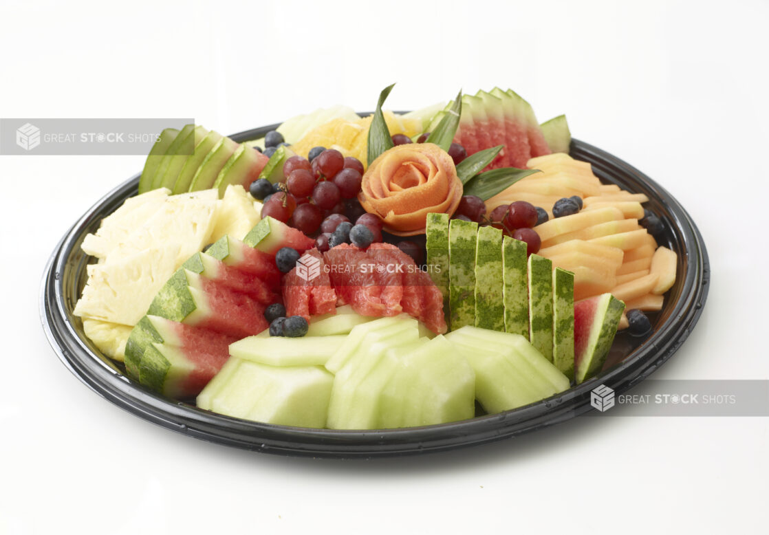 Fresh sliced fruit platter with honey dew melon, watermelon, cantaloupe, pineapple, grapes and blueberries on a round black catering tray