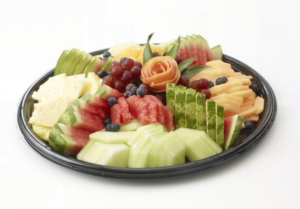 Fresh sliced fruit platter with honey dew melon, watermelon, cantaloupe, pineapple, grapes and blueberries on a round black catering tray