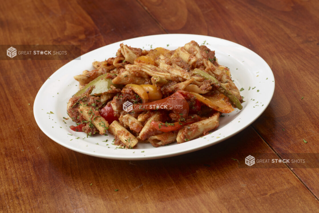 Penne pasta with Bolognese sauce and bell peppers in a round white bowl on a wooden background