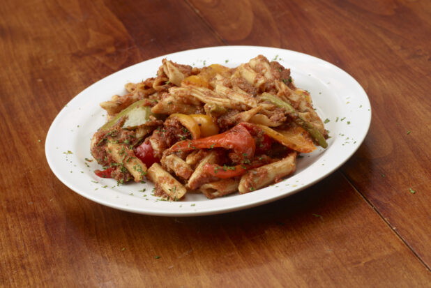 Penne pasta with Bolognese sauce and bell peppers in a round white bowl on a wooden background