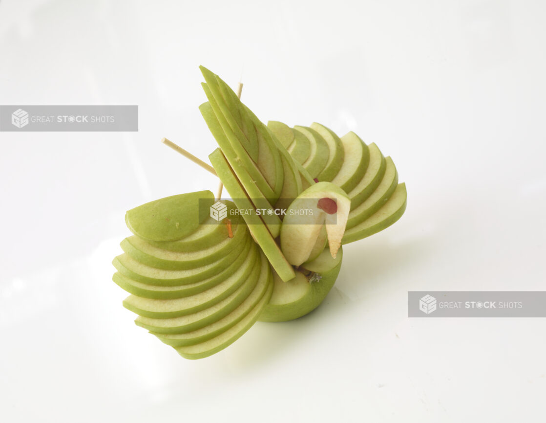 Green apple sliced/designed to look like a bird on a white background