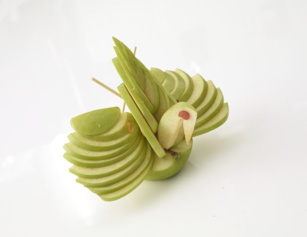 Green apple sliced/designed to look like a bird on a white background