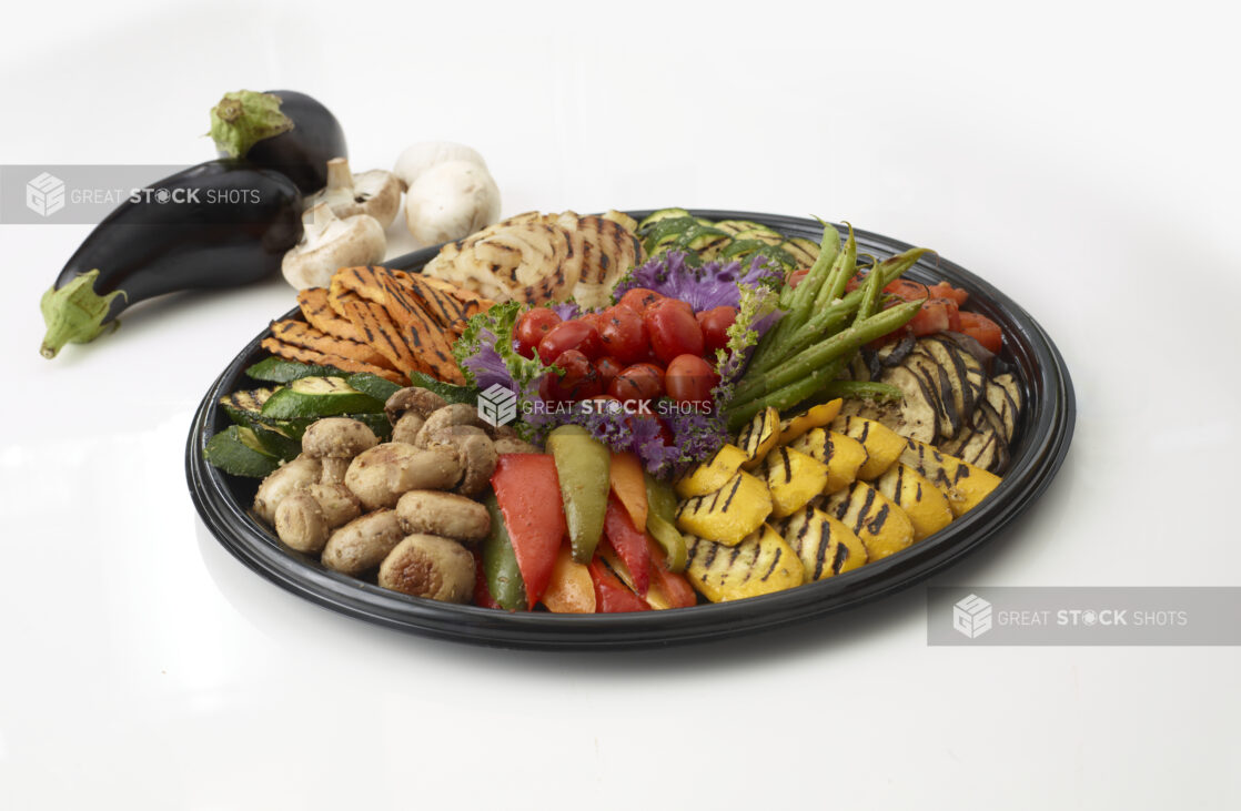 Roasted vegetable platter on a round black tray with whole mushrooms and zucchini in the background